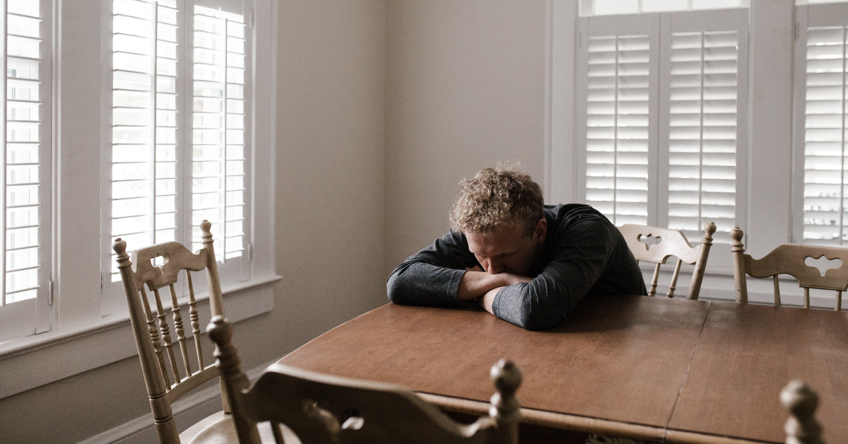 A man in a bathrobe sitting at a kitchen table with his head on the table going through heroin withdrawal