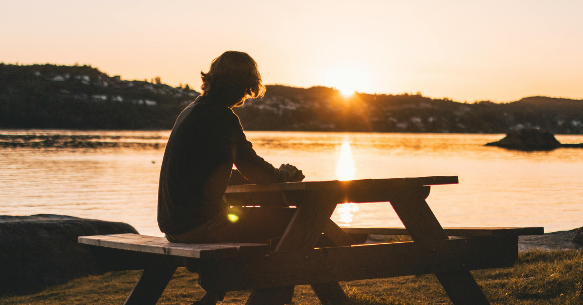 A man sitting on a picnic table bench, overlooking water while in IOP at Milton